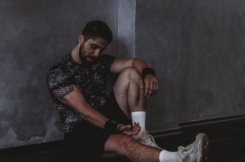 A muscular man in a gym environment taking a moment of rest, reflecting in a dark moody setting.